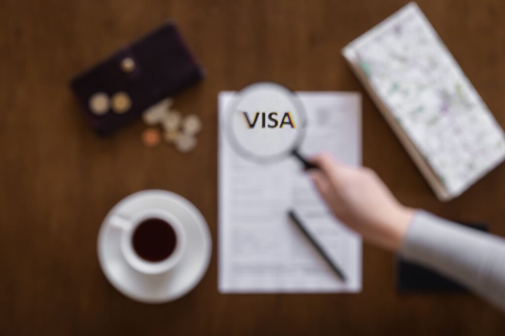 Magnifying glass positioned over a visa application form on a wooden table with coffee and personal items around it