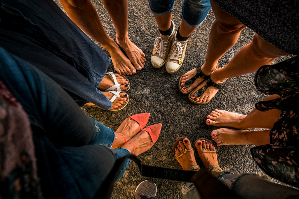 A circle of feet in different types of shoes.